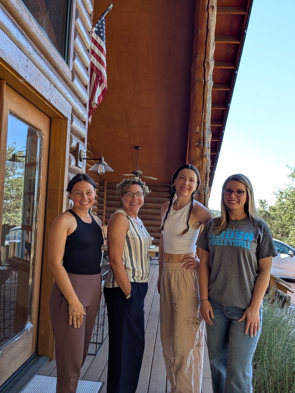 A group of four women smiling together on a cabin porch during a Studio Willow experience